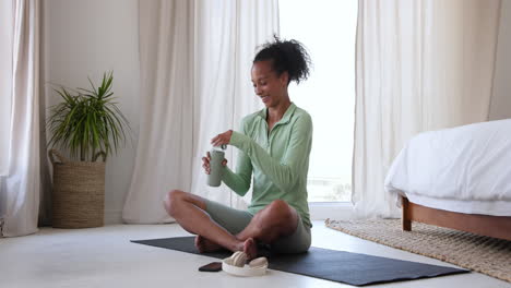 woman in green activewear drinking water on yoga mat at home, relaxing after workout