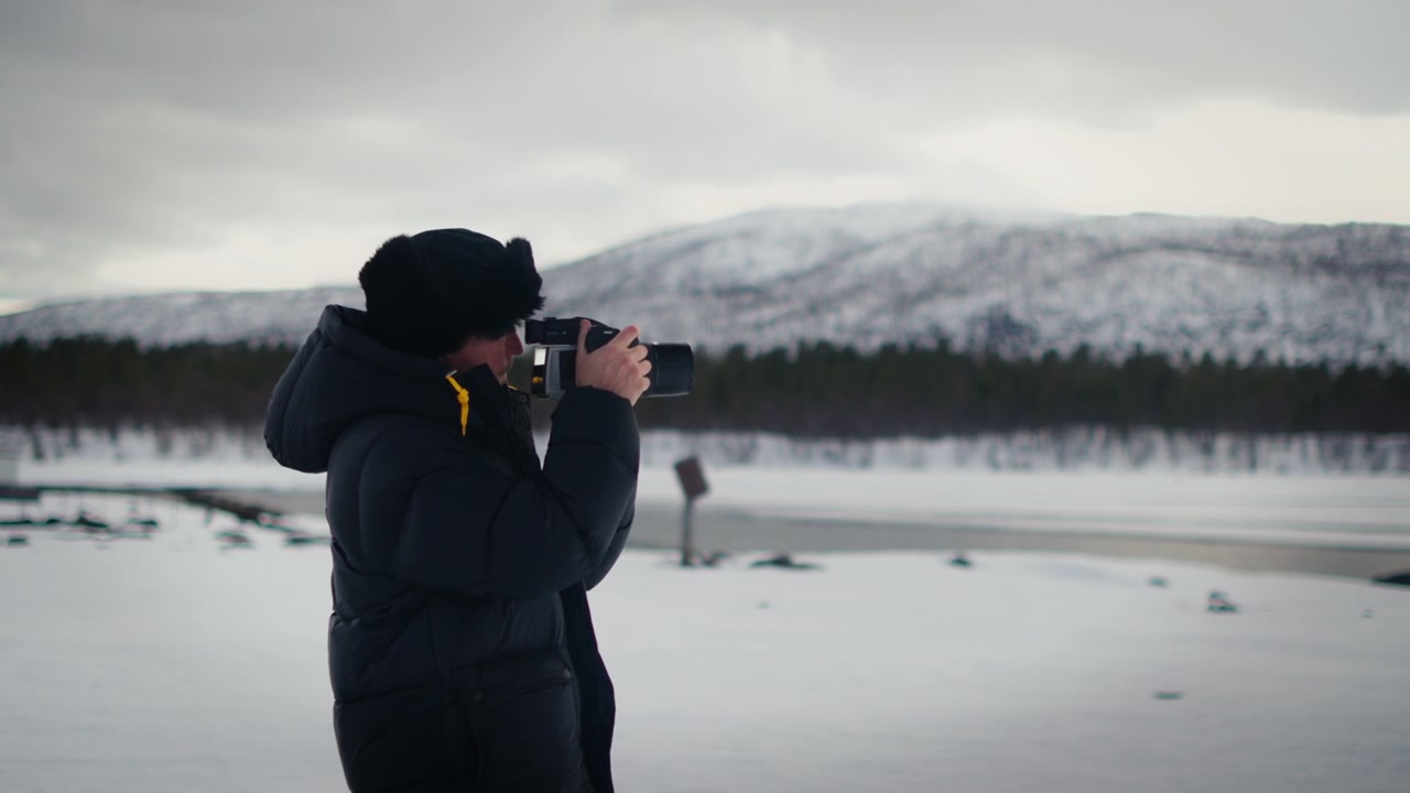 A photographer walks into frame and takes pictures of a snowy mountain landscape in winter. Ideal for travel, nature, photography and outdoor adventure content.