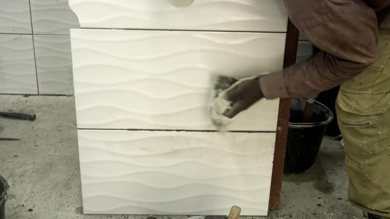 Man wiping off excess cement off white wall tile with cloth