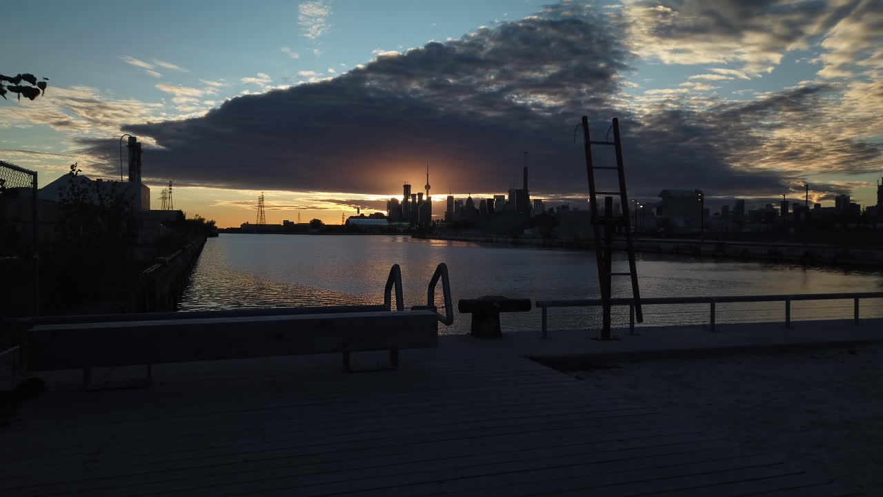 Sunset at Leslie Lookout Park, with shipping channel in foreground, sun glowing behind Toronto city skyline in the distance, wide shot