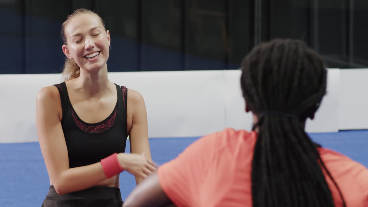 Young woman drinking smoothie after padel tennis match, relaxing with friend, on indoor court