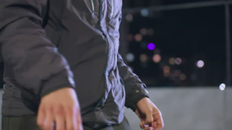 close-up of athlete's hands and knee during nighttime football juggling practice on an urban field with bokeh light effects and city buildings in the background