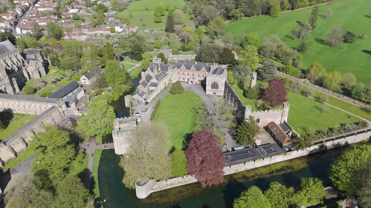 Aerial orbit of medieval palace complex with stone towers, moat and formal lawns, highlighting historic architecture and tranquil green surroundings for heritage storytelling