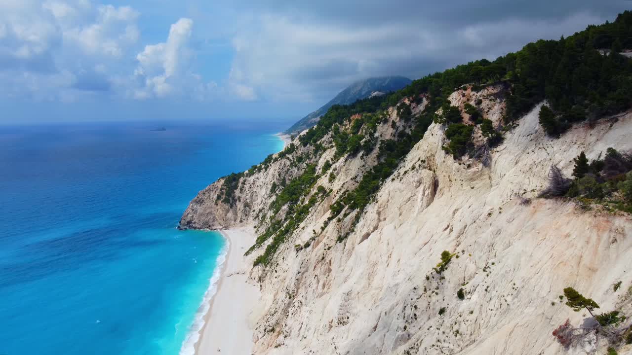 Vista aérea de montanhas brancas e vegetação verde exuberante cercadas por água do mar azul profundo na Praia de Egremni, ilha de Lefkada, sob céu chuvoso.