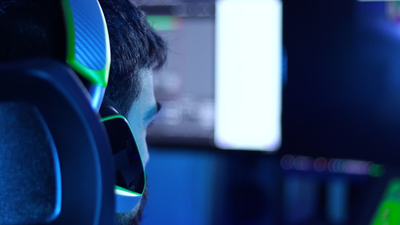 vista trasera de un jugador, adulto joven streamer frente a una pantalla de pc con un auricular de jugador verde, toma de 4k