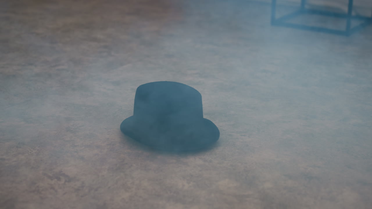 black top hat falling onto dusty studio floor, thick smoke swirling around stool frame, sun light streaming through tall windows, creating ethereal vintage ambiance with textured concrete surface