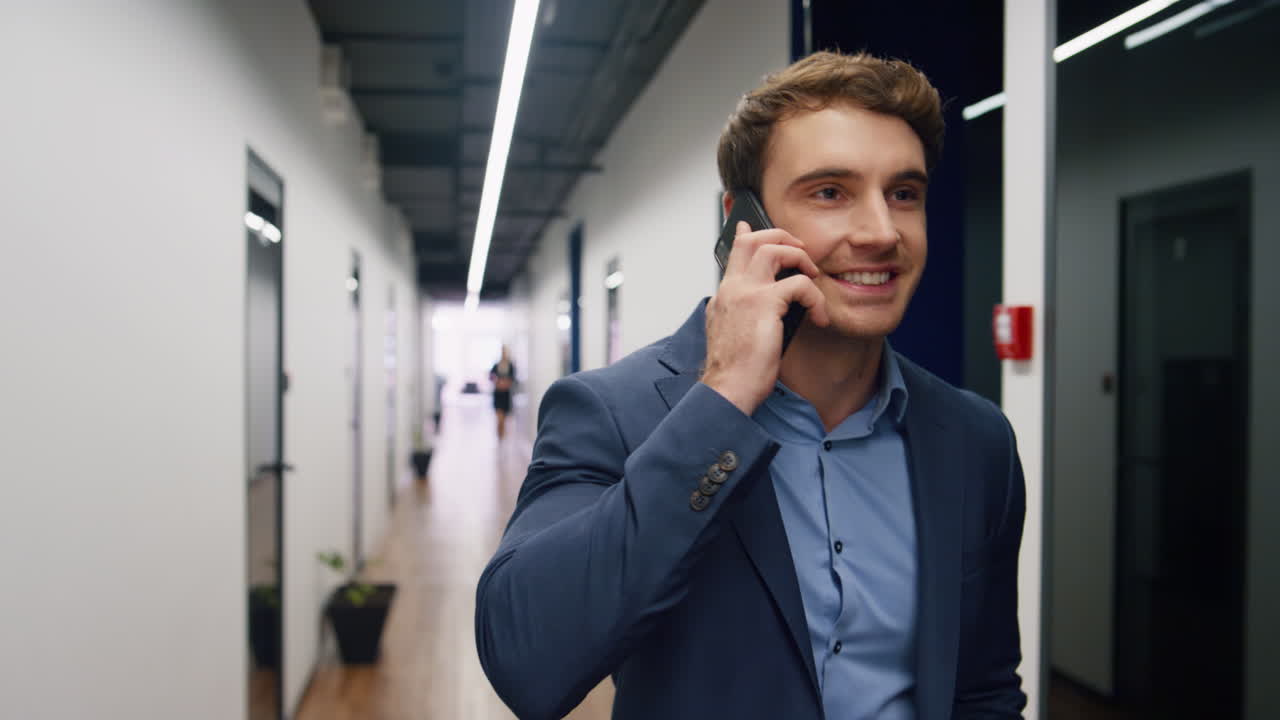 Begejstret medarbejder taler i smartphone på kontoret. Smilende iværksætter deler gode nyheder.