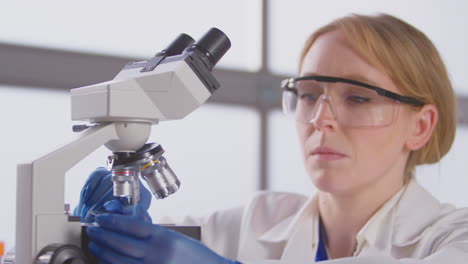 trabajadora de laboratorio que pone una diapositiva bajo el microscopio para su análisis