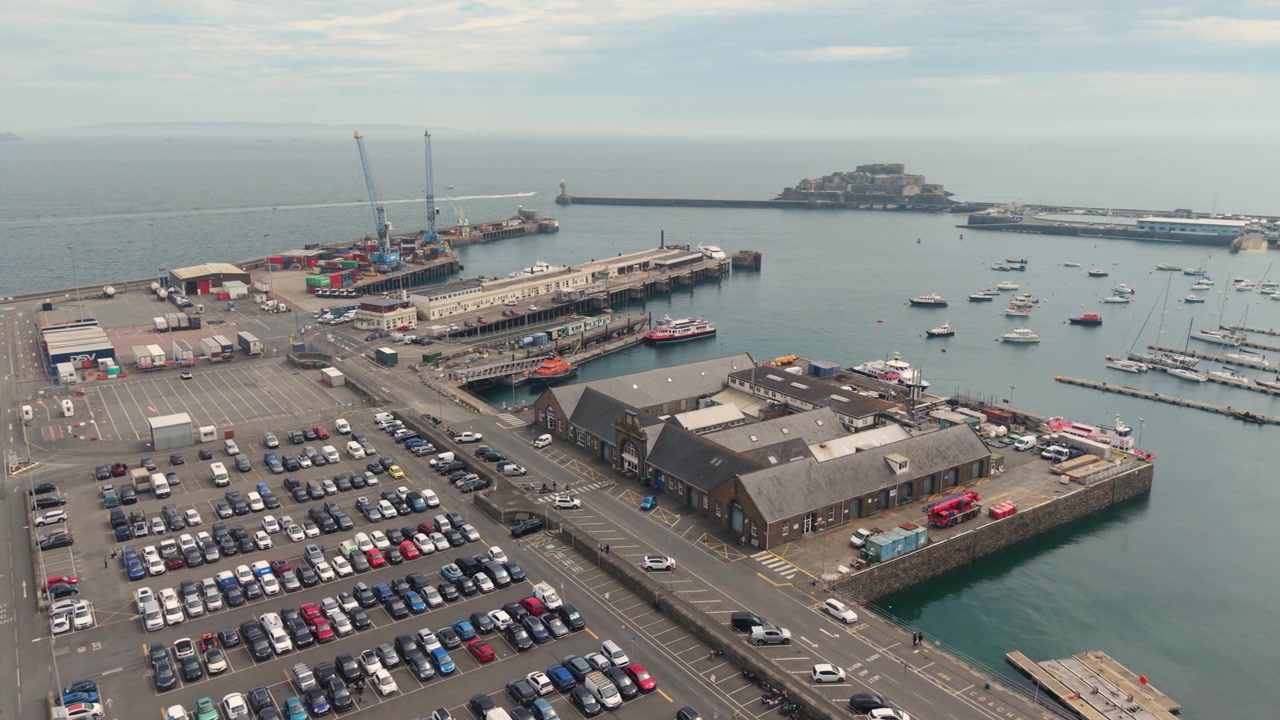 Pelabuhan St Peter Port, Guernsey, Kepulauan Channel. Rekaman drone panning tinggi pelabuhan luar, Pantai Utara, Dermaga Cambridge, dok, dan Kastil Cornet pada hari berkabut