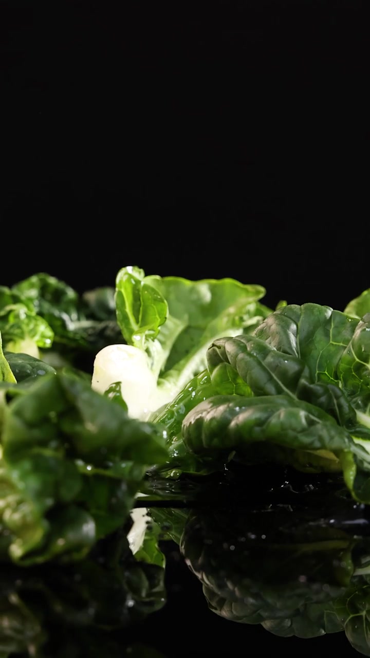 Bok choy croccante cade su una superficie nera riflettente, con goccioline d'acqua che schizzano, sotto un'illuminazione drammatica da studio con una fotocamera statica e acquisizione ad alta velocità