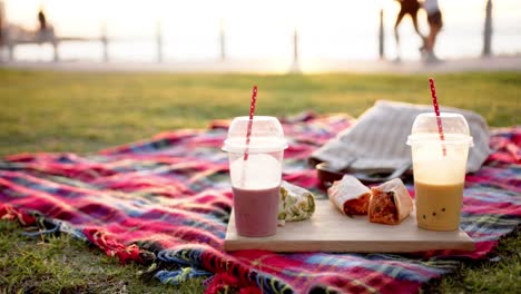 close up of blanket with smoothies and tortillas at picnic on promenade by the sea, slow motion