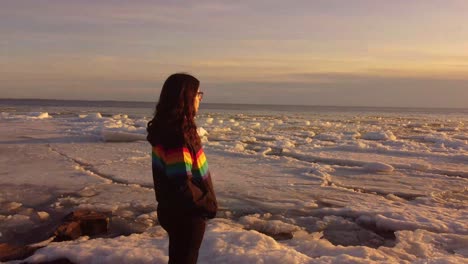 mujeres jóvenes con chaqueta de colores de orgullo en una roca en medio de un lago congelado