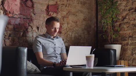 A-young-man-in-a-shirt-is-sitting-at-a-table-with-a-laptop-and-typing-on-the-keyboard.-A-student-can-study-remotely.-A-businessman-conducts-his-business-remotely