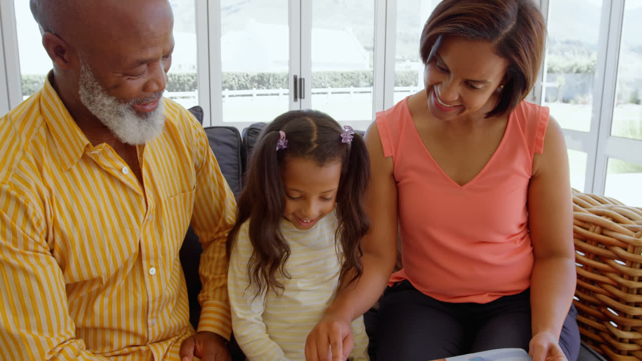 vista frontal de una familia negra sentada en el sofá y buscando un álbum de fotos en un hogar cómodo 4k