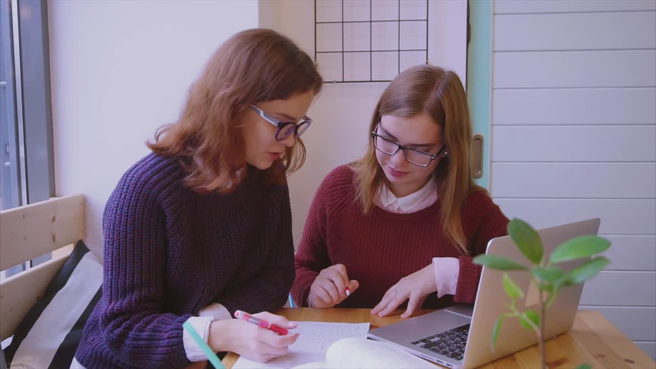 dos mujeres jóvenes estudiando juntas en una cafetería