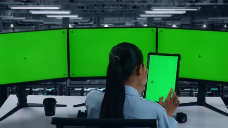 vista trasera de una mujer asiática trabajando con una tableta y varios monitores de computadora con una pantalla verde simulada en el centro de datos