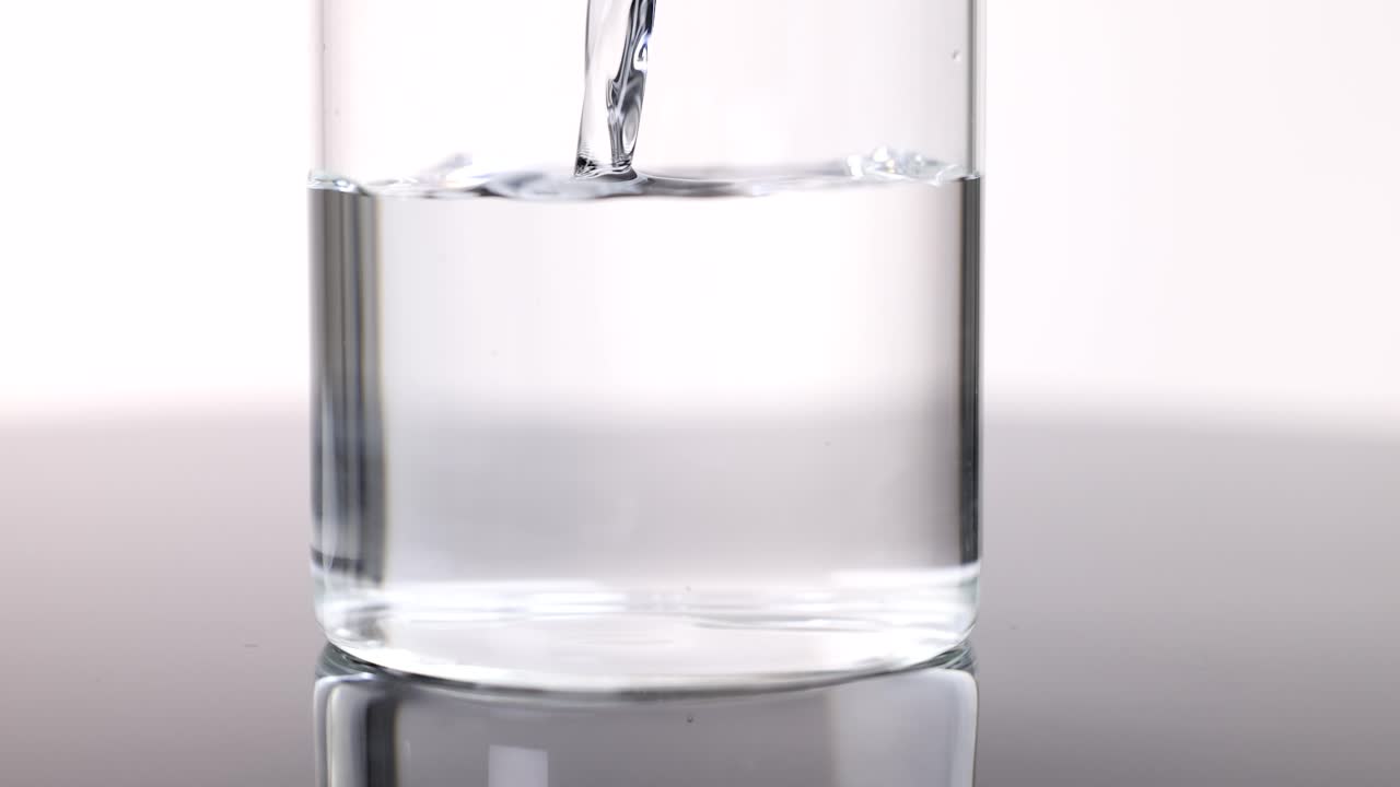 Clear water poured into glass on reflective surface, bright backlighting, static camera, scientific context