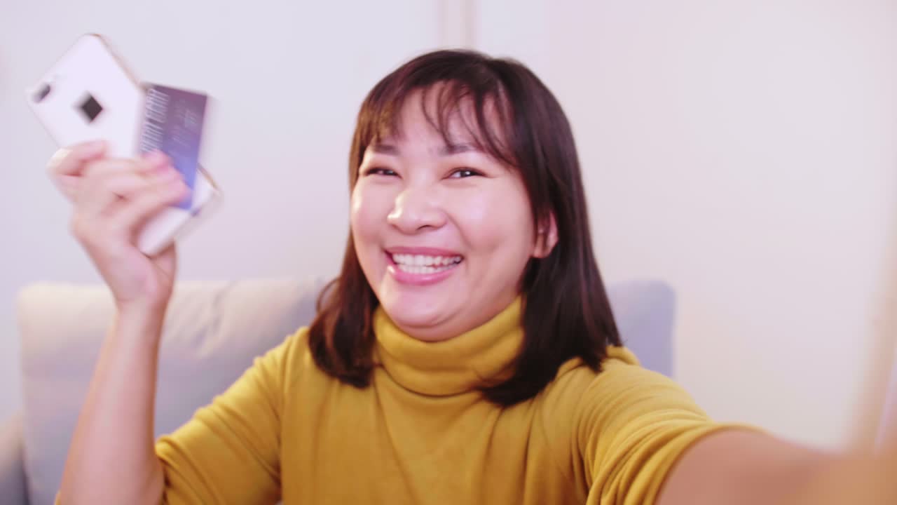 아시아 여성들은 여행 예약을 성공적으로 마친 후 신용 카드와 휴대폰을 보여주는 친구들과 화상 통화를 하며 행복하고 미소 짓습니다.