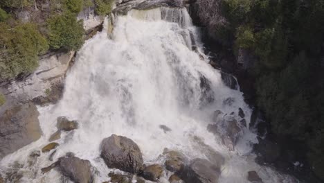 Powerful-waterfall-cascading-over-rocks-surrounded-by-lush-green-trees,-aerial-view