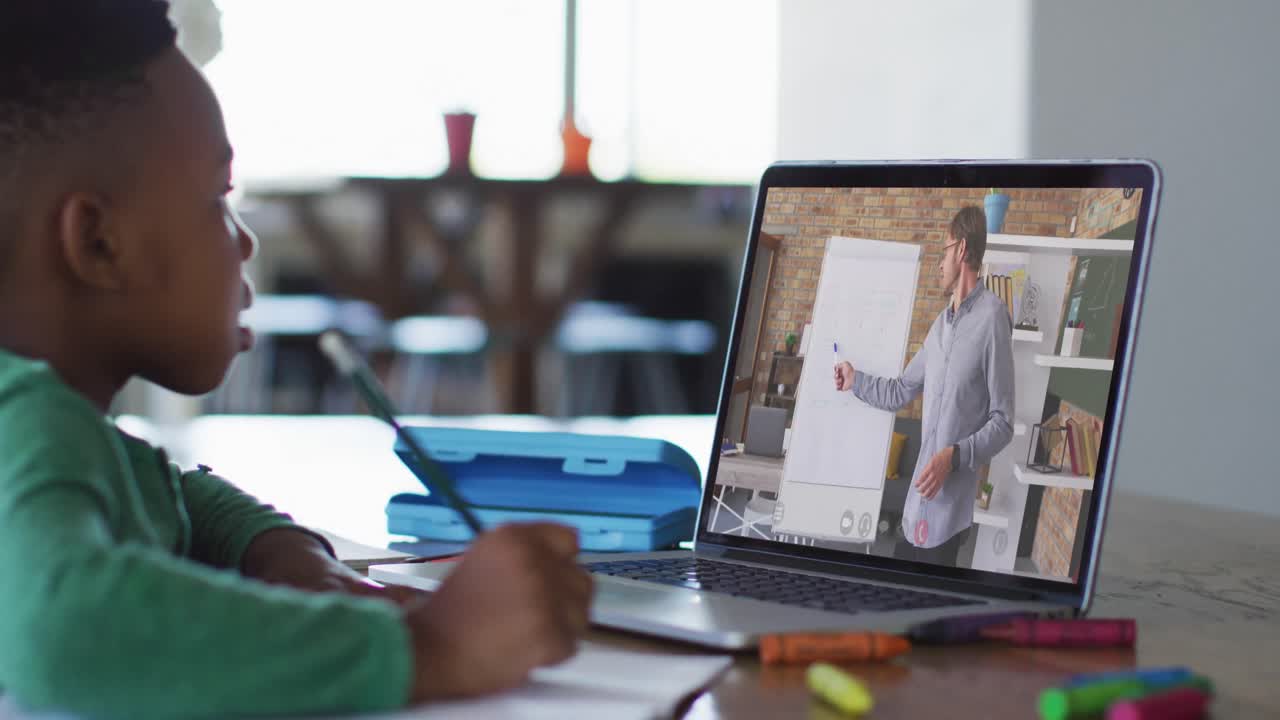 niño afroamericano haciendo una videollamada en una computadora portátil mientras hace la tarea en casa