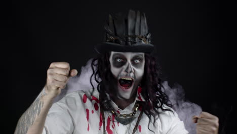 sinister man with halloween skeleton makeup in shirt with blood celebrating, pointing at camera