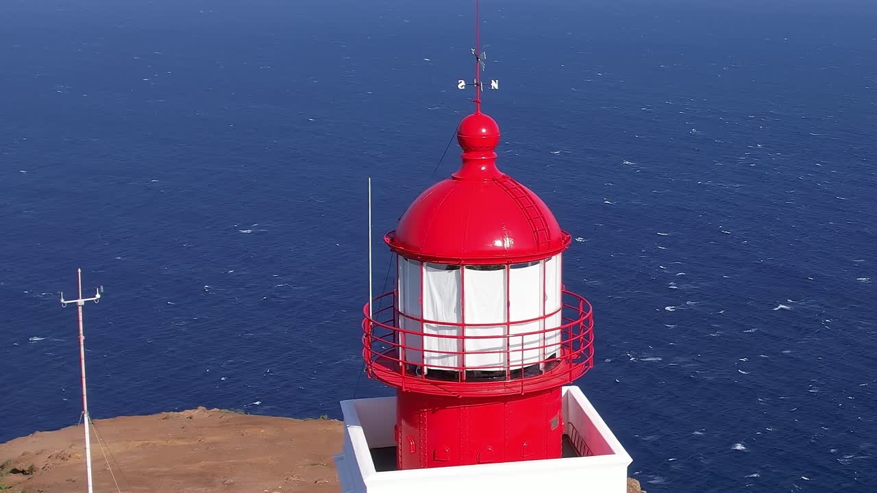 Red lighthouse stands tall against the blue ocean in Madeira, Portugal