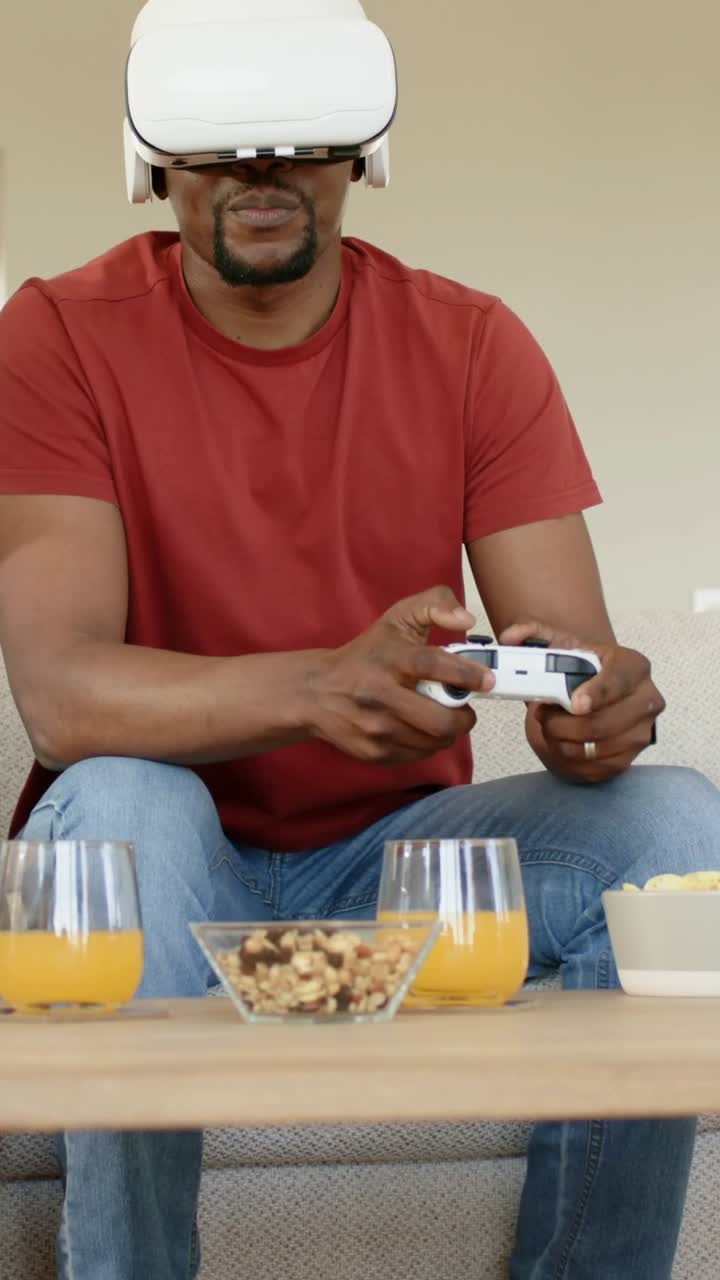 Vertical video: Pressing controller buttons, man in red tee wearing VR headset playing game at home