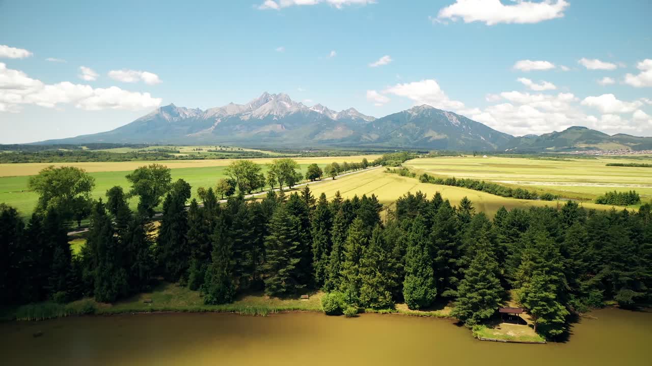 Aerial footage of a lake with spruce trees and mountain range in the background