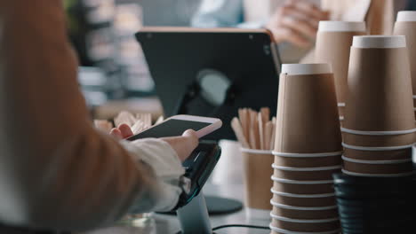 Schöne-Barista-Frau-Bedient-Kunden-Per-Smartphone-Und-Macht-Kontaktloses-Bezahlen,-Indem-Sie-Kaffee-Kauft-Und-Im-Café-Geld-Ausgibt