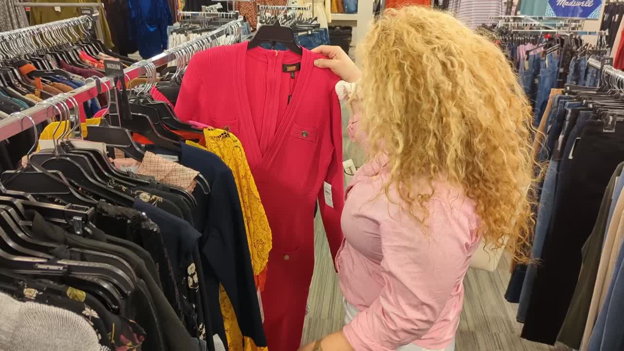 아름다운 라틴 여성은 옷을 쇼핑하고 그녀가 좋아하는 드레스를 꺼내고 카메라를 보며 큰 미소를 짓습니다.