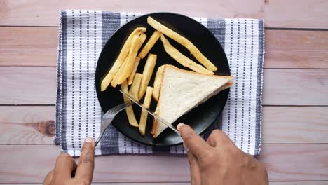 hand cutting a sandwich and fries on a plate