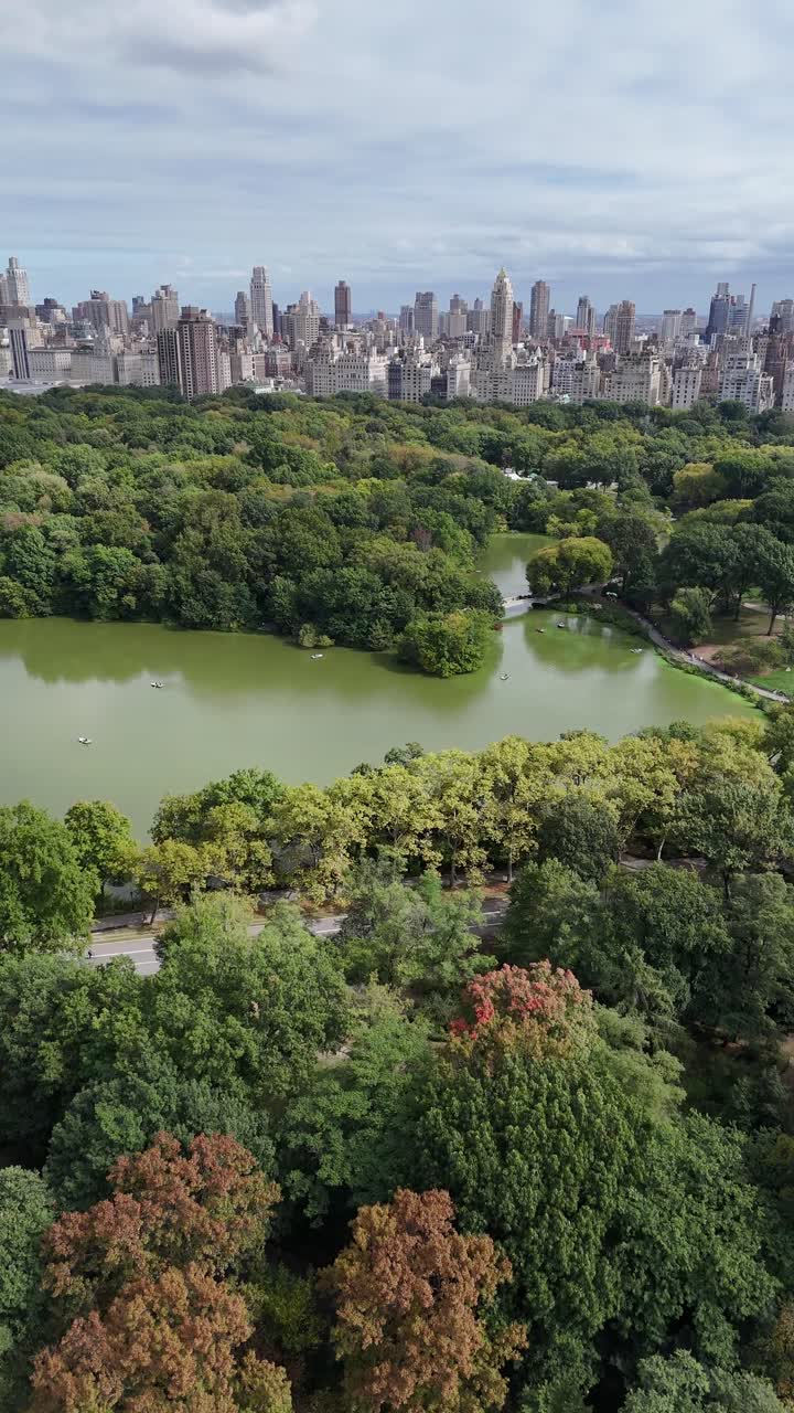 A stunning vertical orientation drone aerial view of Central Park lake and W 72nd Street in New York City, blending Manhattan’s vibrant skyline with the serene greenery of Central Park.