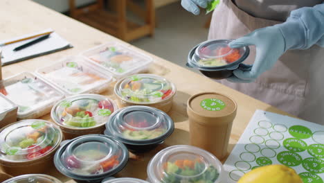 trabajador de servicio de entrega de alimentos poniendo pegatinas en contenedores con comidas ecológicas
