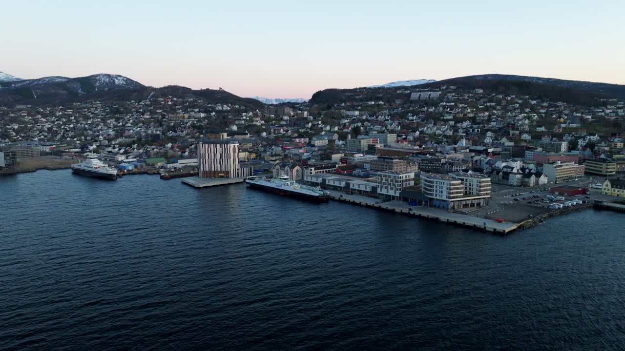 Malerische Luftaufnahme der Küstenlinie von Harstad in Nordnorwegen. Blick auf die Skyline der Stadt, angedockte Schiffe und Häuser an den Hängen in der Abenddämmerung. Ideal für Reise- und Skandinavien-Inhalte.