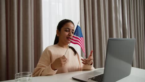 Happy-brunette-girl-in-light-pink-on-a-video-call-while-learning-English-at-home-online-in-a-modern-apartment.-Learning-foreign-languages-online-at-home