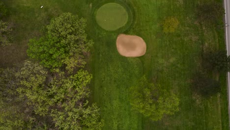 aerial view of green golf course next to a road with cars