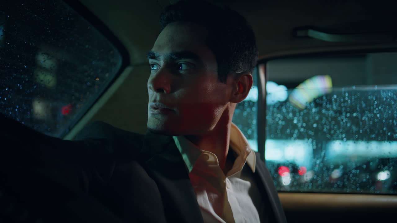 Strict businessman looking car window back rainy night. Serious man sitting taxi