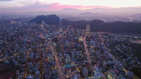 Luftpanorama-Stadtbild-Von-Santiago,-Chile,-Providencia-Bei-Rosafarbenem-Sonnenuntergang,-Andengebirgshintergrund,-Straßenbeleuchtung-Der-Stadt-Und-Wolkenkratzern