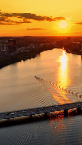 setting sun coloring the sky in orange above the charles river in boston, massachusetts, usa. drone footage above the waterscape and bridge across it. vertical video