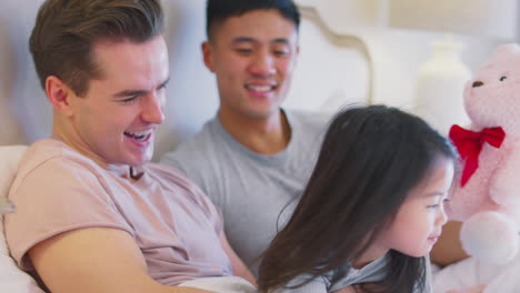 family with two dads in bed at home playing game with daughter and her soft toy