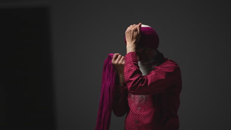 Fotografía-De-Estudio-Con-Iluminación-Tenue-De-Un-Hombre-Sikh-Mayor-Con-Barba-Atando-Una-Tela-Para-Un-Turbante-Contra-Un-Fondo-Oscuro,-Filmada-En-Tiempo-Real-2