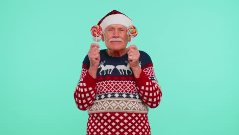 grandfather in christmas sweater holding candy striped lollipops hiding behind them fooling around