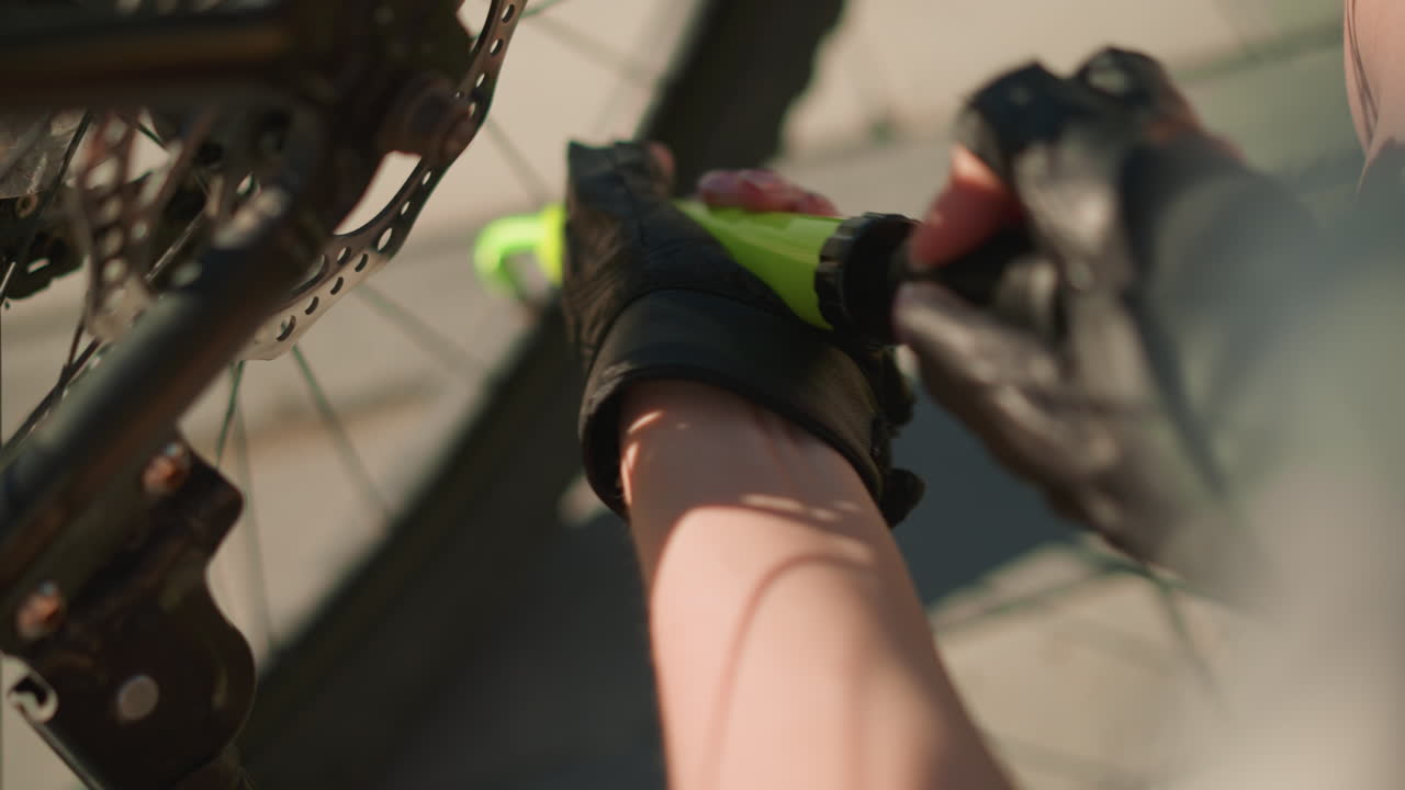primer plano de una mano con guantes bombeando firmemente aire en el neumático de la bicicleta utilizando una boquilla verde bajo la luz del sol brillante, enfoque detallado en las manos y la bomba, con un suave borrón de fondo