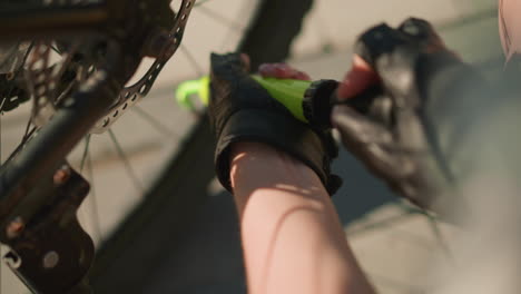 close-up of gloved hand firmly pumping air into bicycle tire using green nozzle under bright sunlight, detailed focus on hands and pump, with soft blur of background