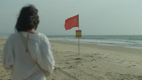 bandera de advertencia roja en una playa vacía con mujeres jóvenes caminando, tiempo nublado