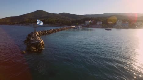 Aerial:-Small-fishing-town-with-Greek-flag-on-Samos-island,-Greece