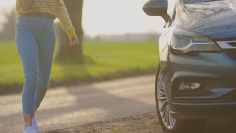 mujer pidiendo ayuda por teléfono después de una avería de coche en una carretera de campo con un neumático perforado