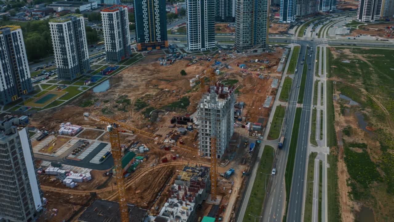 grúas de torre de hiperlapso aéreo que trabajan en un sitio de construcción en la ciudad. desarrollo de construcciones disparadas por drones en un día soleado. maquinaria y trabajadores empleados. constructores trabajan en edificios residenciales