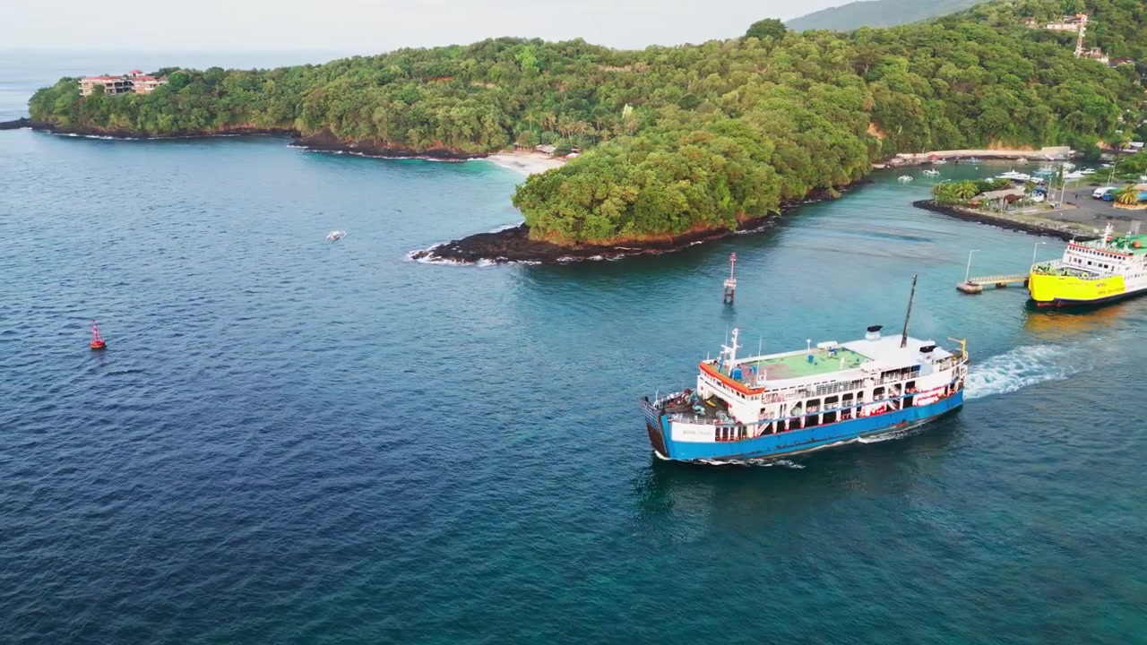 Traghetto che parte da un porto di un'isola tropicale attraverso acque costiere limpide e blu circondato da una costa tropicale e un paesaggio insulare panoramico, riprese aeree con drone