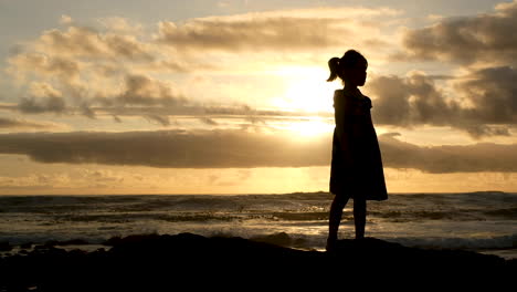 spontaneous singing of young innocent girl on coastline, breaking waves and golden sunset sky background